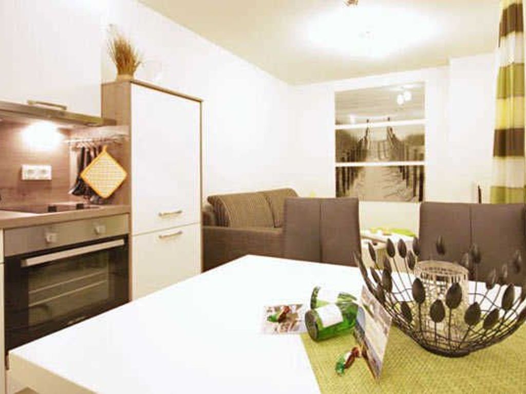 A modern kitchen with a built-in oven, a dining area with a white table, and a seating area with a sofa.