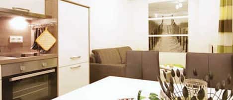 A modern kitchen with a built-in oven, a dining area with a white table, and a seating area with a sofa.