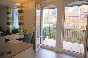 Une pièce comprenant une table à manger, des chaises, un coin cuisine et une porte-fenêtre coulissante donnant sur une terrasse extérieure.