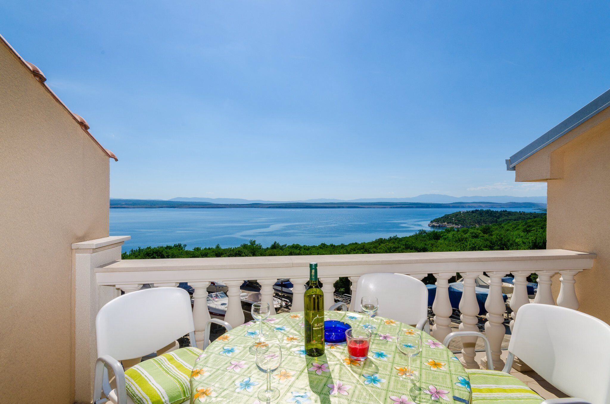A balcony with a table set for two, overlooking a scenic view of the sea and greenery.