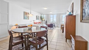 A spacious living area with a dining table, chairs, a sofa, and a large window providing a view.