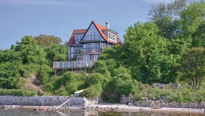 A two-story house with a balcony, surrounded by dense greenery and a body of water.