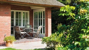 Ein Gebäude aus Ziegeln mit einem Strohdach, einer Terrasse mit zwei Stühlen und einem Tisch.