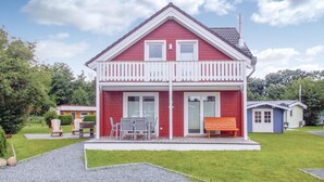 A red two-story house with a balcony, a small porch with outdoor furniture, and a clear sky. - Beach front home in Süssau/Ostsee (Süssau/Ostsee)