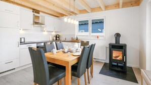 A modern kitchen with white cabinets, a wooden dining table with chairs, a built-in stove, and a window with a view of the sea. - Beach front home in Süssau/Ostsee (Süssau/Ostsee)