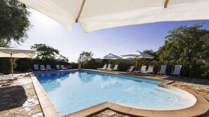 A swimming pool with lounge chairs and umbrellas, surrounded by stone tiles and greenery. - Holiday apartment with climate control system (Alghero)