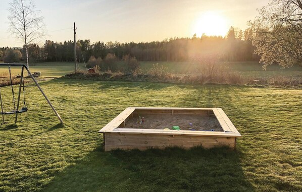 A sandbox in a grassy field with a swing set nearby.