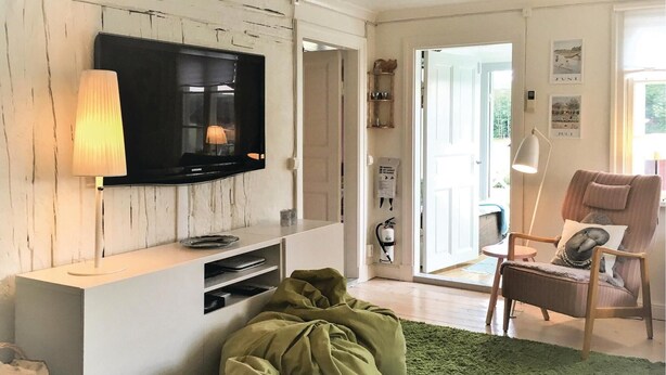 A living room with a flat-screen TV mounted on a white wall, a green sofa, a small round table, and a green rug. - Lovely home in Sollebrunn with WiFi (Sollebrunn)