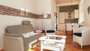 Ein Wohnzimmer mit einer Couch, Sesseln, einem Couchtisch und einer Küche im Hintergrund.