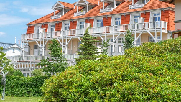 Ein mehrstöckiges Hotel mit Balkonen, einem Garten und blauem Himmel.