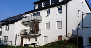 A multi-story residential building with balconies, a garage, and a small garden area.