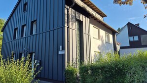 Ein modernes Gebäude mit dunkler Fassade, einem gut sichtbaren Eingang und einem Schild, das einen Wohnbereich kennzeichnet.