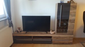 Una sala de estar con televisor de pantalla plana sobre un soporte de madera, una pequeña estatua y un espejo.