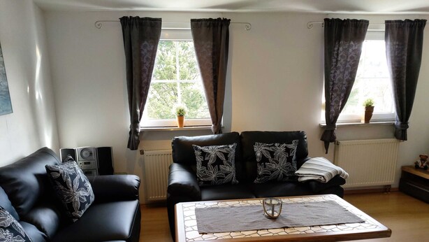 Ein Wohnzimmer mit einer schwarzen Ledersofa, einem Holztisch und einer Heizung.