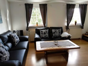 A living room with a black leather sofa, a wooden coffee table, and a radiator.