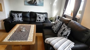 Ein Wohnzimmer mit einem schwarzen Ledersofa, einem Couchtisch mit einer Glasvase und einem Gemälde an der Wand.