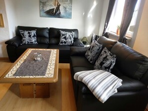A living room with a black leather sofa, a coffee table with a glass container, and a painting on the wall.
