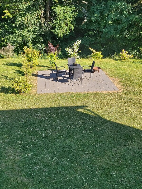 Un patio exterior con mesa y sillas, rodeado de césped y árboles.