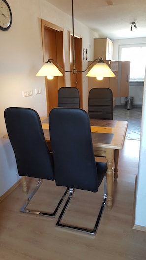 Un comedor con una mesa de madera, cuatro sillas, dos lámparas colgantes y un reloj en la pared.