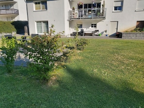 A residential building with a balcony, a small garden area, and a patio with outdoor furniture.