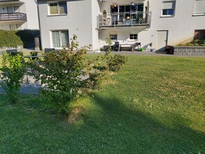 Ein Wohngebäude mit Balkon, einem kleinen Garten und einer Terrasse mit Gartenmöbeln.