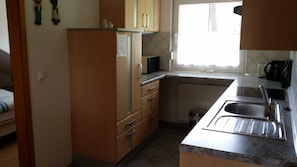 A compact kitchen with a refrigerator, microwave, sink, and a window with a view.