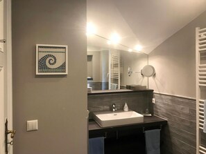 Un baño con pared de azulejos, un lavabo, un espejo y un perchero para toallas.