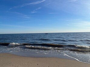 Une plage avec des vagues, un bateau à l’horizon et un ciel dégagé.