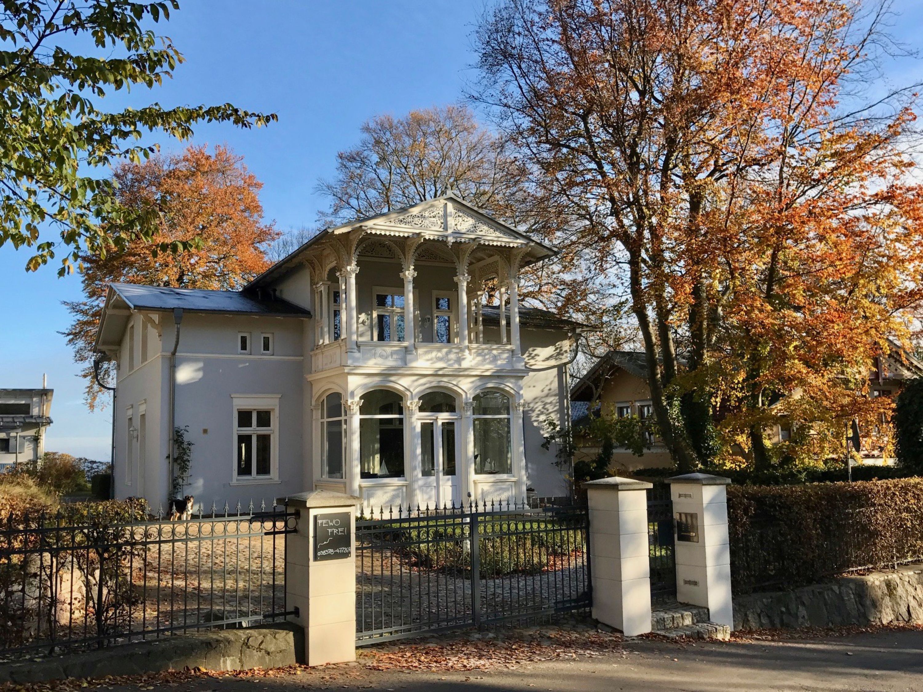 Een tweelaags gebouw met een balkon en een hek, met een bord waarop de naam 'TEWO TREI' staat.