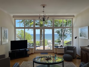 Una sala de estar con un ventanal grande, televisor, candelabro y vista al mar.
