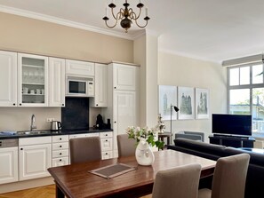 A modern kitchen with white cabinets, a dining table with chairs, a chandelier, and artwork on the wall.