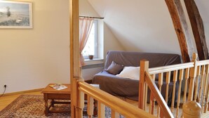 A cozy loft bedroom with a sloped ceiling, a brown sofa, a wooden staircase, and a view of the outdoors through a window. - 3 bedroom stunning home in Chigny (Chigny)