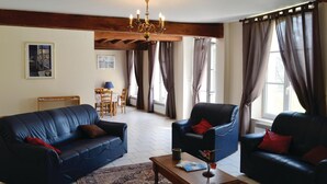 A living room with two leather sofas, a wooden coffee table, a chandelier, and large windows with curtains. - 3 bedroom stunning home in Chigny (Chigny)