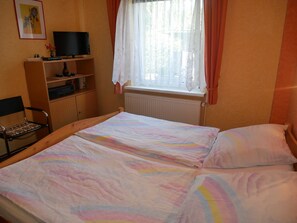 Quarto com cama, cadeira, televisão e janela com cortinas.