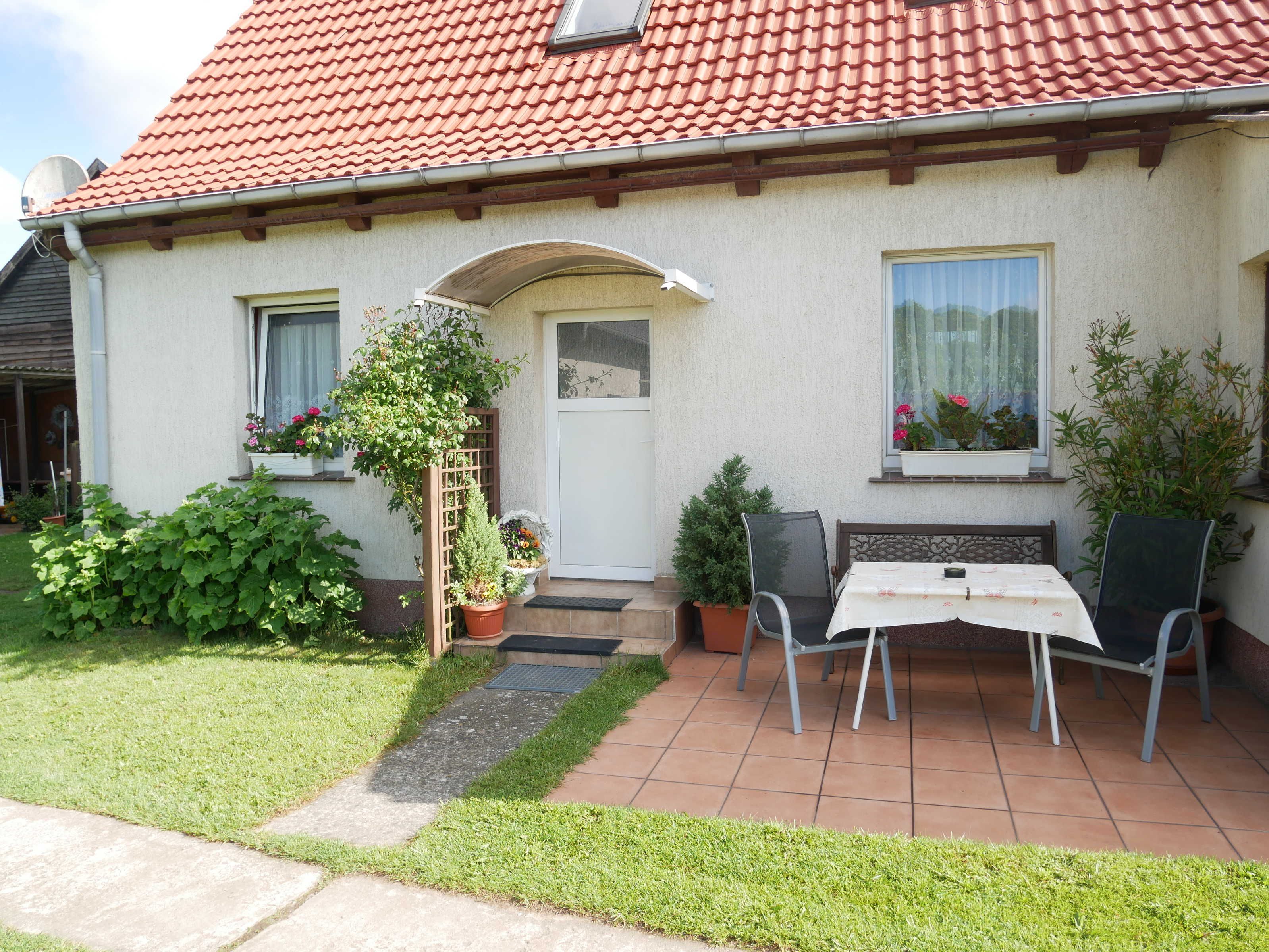 A house with a red-tiled roof, a small front porch, and a patio area with a table and chairs.