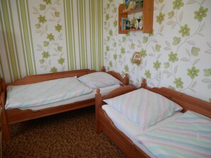 Quarto com duas camas de madeira, cada uma com roupa de cama listrada. Há uma prateleira com vários objetos na parede acima das camas.
