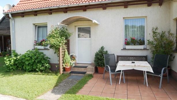 A house with a red-tiled roof, a small front porch, and a patio area with a table and chairs. - Vacation apartment Kasch - Holiday apartment in the countryside (Krummin)