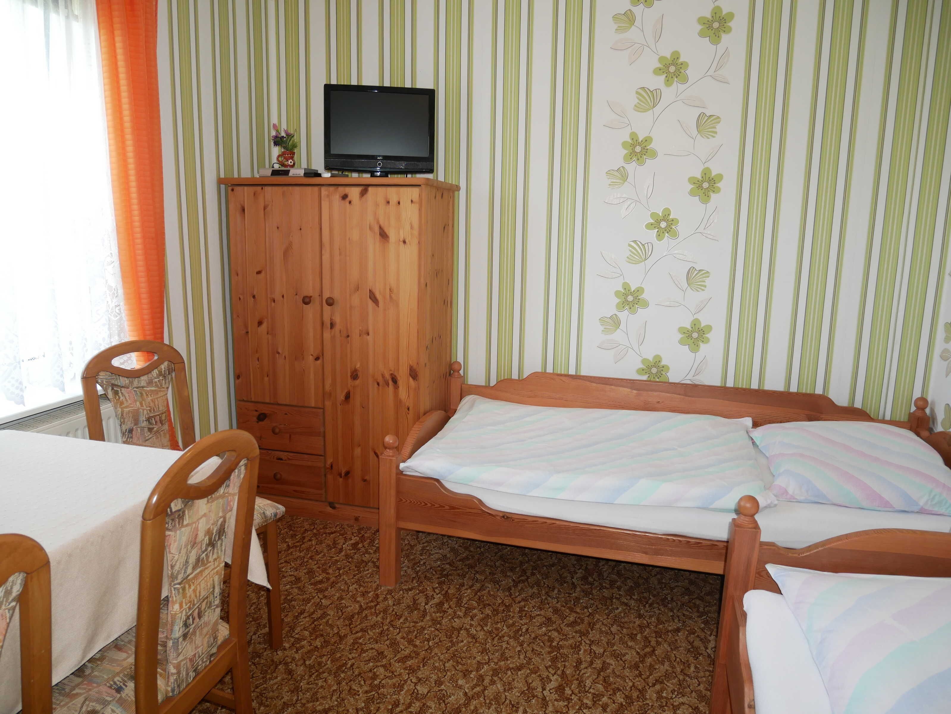 Une pièce comprenant un lit, une armoire en bois avec un téléviseur, une chaise et un mur à rayures.