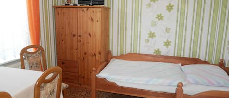 A room with a bed, a wooden cabinet with a television, a chair, and a striped wall.
