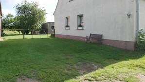 A two-story building with a red-tiled roof, a fenced yard, and a bench outside. - Vacation apartment Kasch - Holiday apartment in the countryside (Krummin)