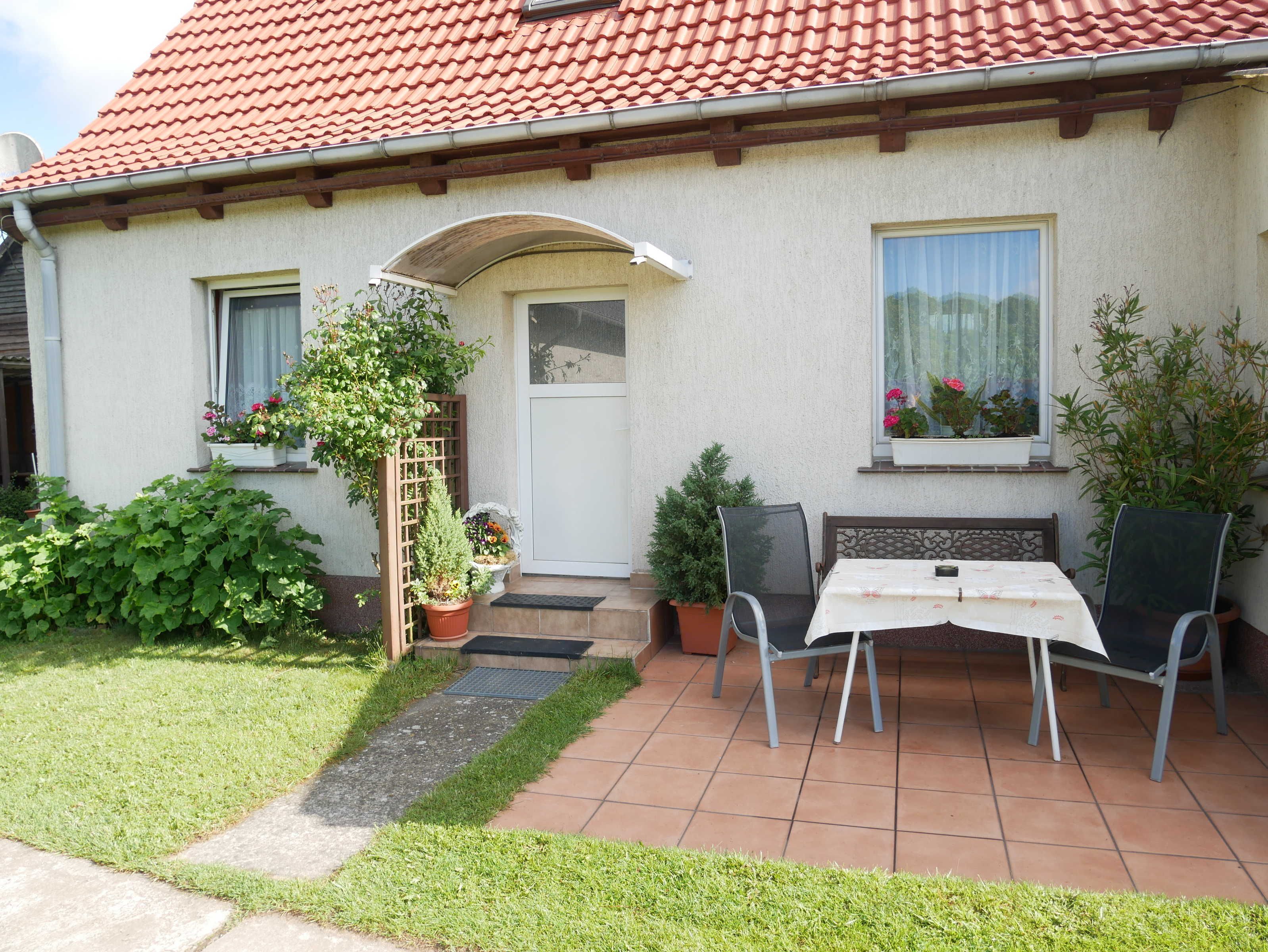 Une maison avec un toit recouvert de tuiles rouges, une porte blanche et une petite terrasse avec une table et des chaises.
