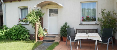 A house with a red-tiled roof, a white door, and a small patio with a table and chairs.