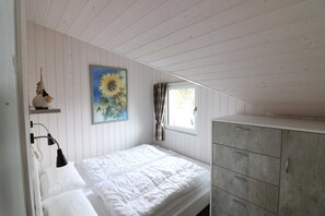 A bedroom with a bed, a dresser, a painting of sunflowers, and a window with curtains.