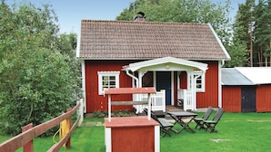 A red wooden house with a tiled roof, a porch with white railings, and a small deck with outdoor furniture. - Gorgeous home in Ruda with kitchen (Ruda)