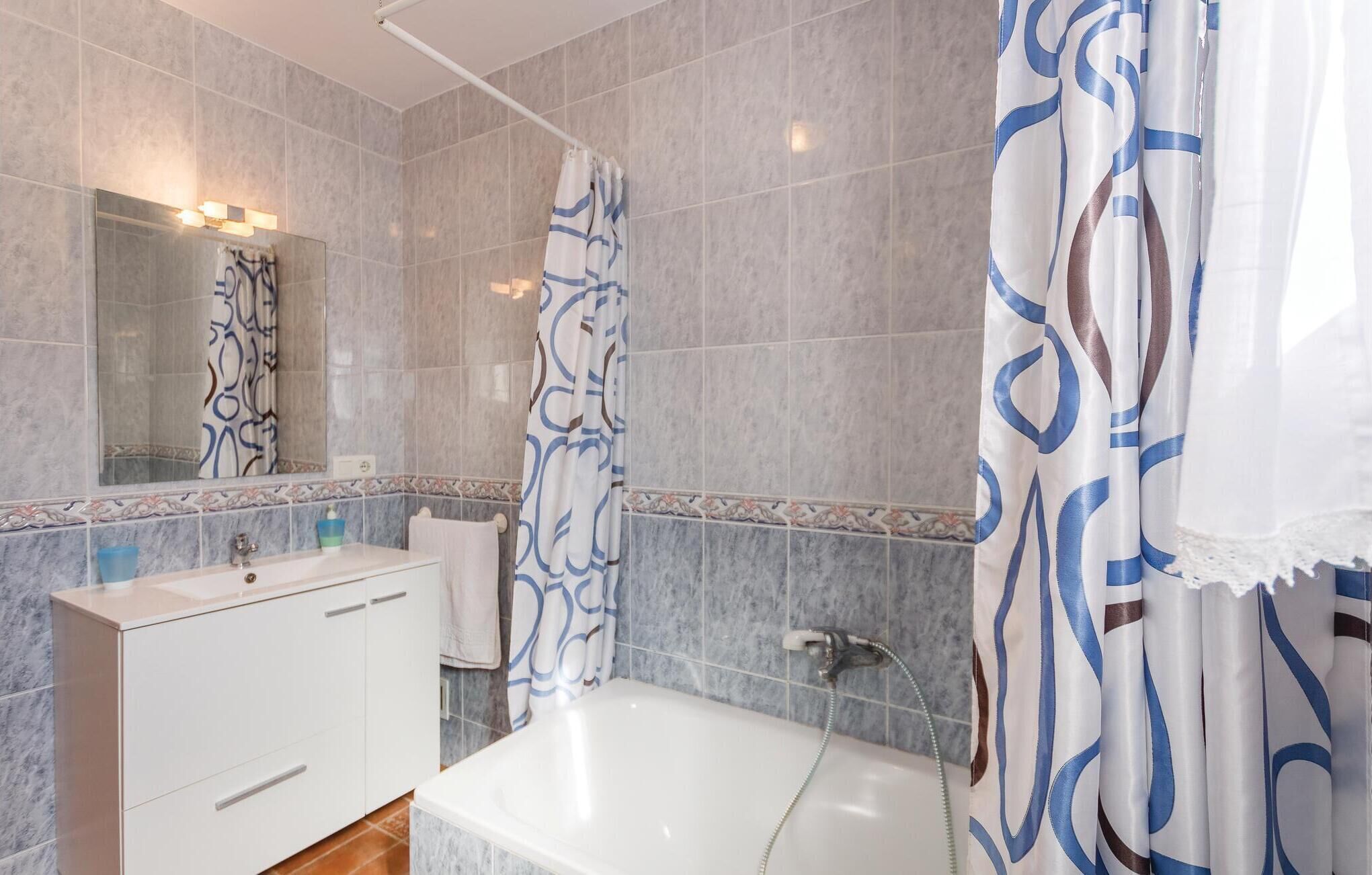 Een moderne badkamer met een witte badkuip, een wastafel met spiegel en douchegordijnen met een patroon.