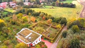 Una casa con techo verde, rodeada por un jardín con diversas plantas y un área cercada.