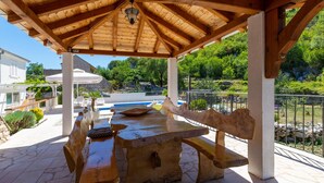 An outdoor wooden pavilion with a stone table and benches, overlooking a swimming pool and greenery. - Amazing home in Blato na Cetini (Blato na Cetini)