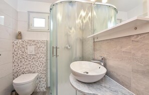Ein modernes Badezimmer mit Duschkabine aus Glas, Toilette und Marmorwaschbecken.