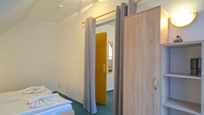 Hotellihuone, jossa on yksi sänky, puinen pöytä, kirjahylly ja ovi, joka johtaa toiseen huoneeseen.