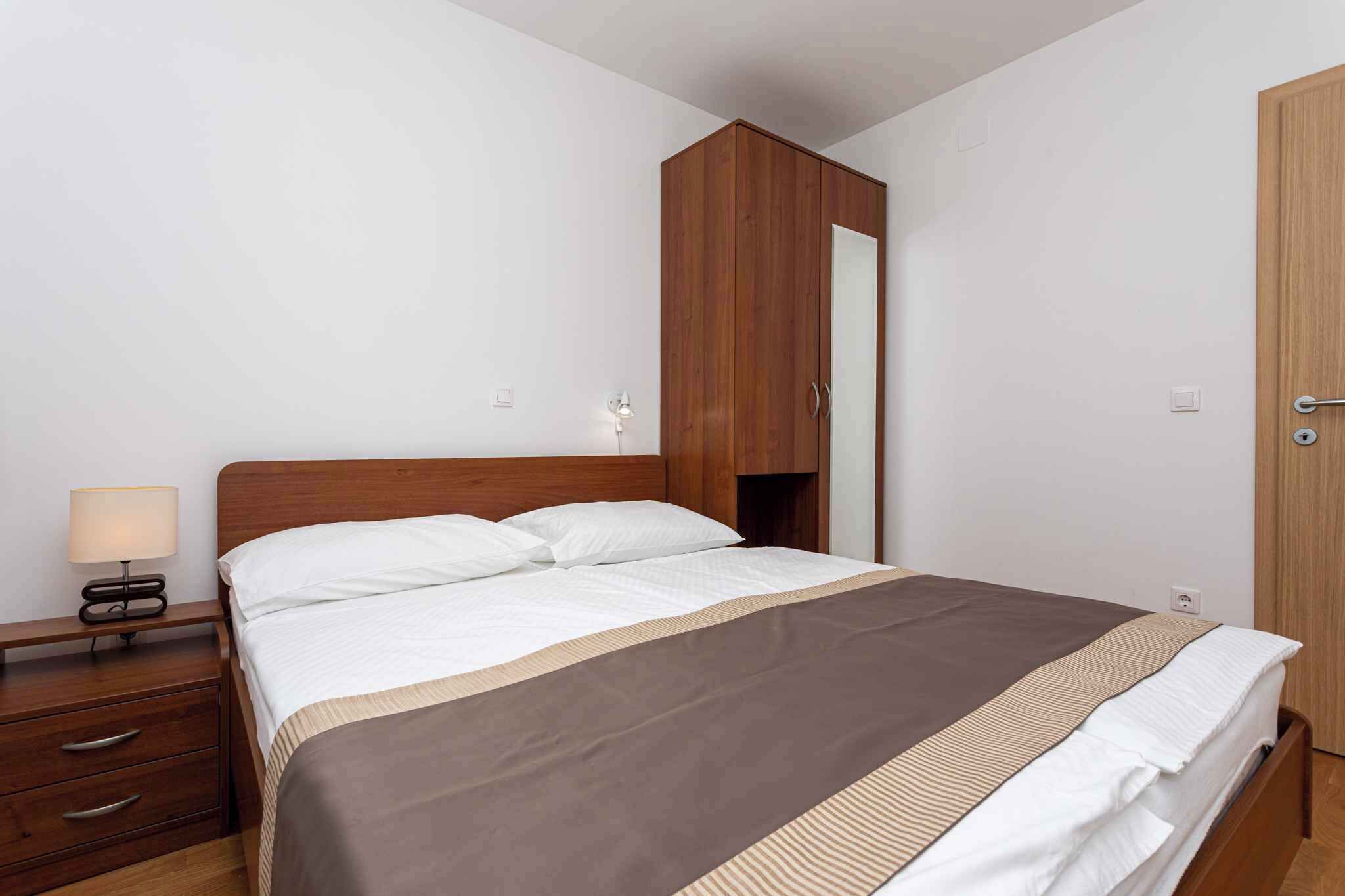 Een keurig opgemaakt bed met een houten hoofdbord, een nachtkastje met een lamp en een garderobe met spiegel.